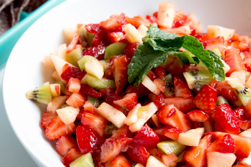 white bowl of strawberry salsa, with kiwi slices mixed in and mint for garnish
