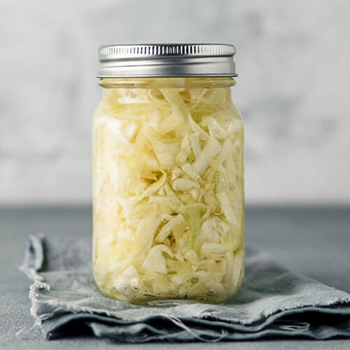 quart sized Mason jar full of sauerkraut secured with a metal band lid, set on top of a gray kitchen towel