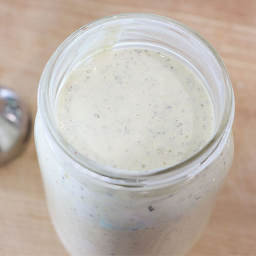 overhead shot of a quart-sized Mason jar filled almost to the brim with healthy, homemade ranch dressing that is white with speckles of green herbs