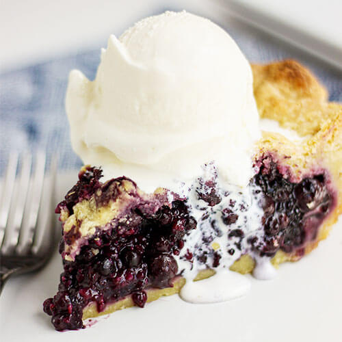 close-up shot of a slice of blueberry pie with a scoop of vanilla ice cream on top, slowly oozing over the edge and onto the plate below
