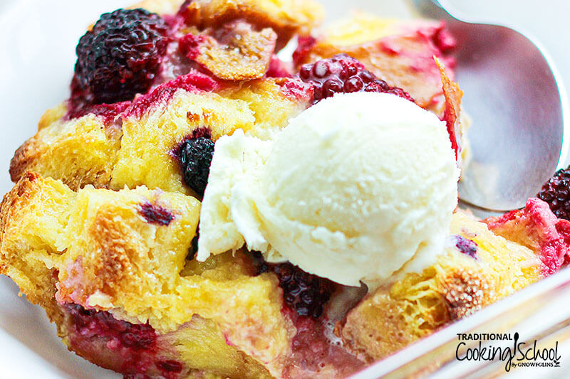 large serving of mixed berry bread pudding topped with a scoop of vanilla ice cream and a spoon