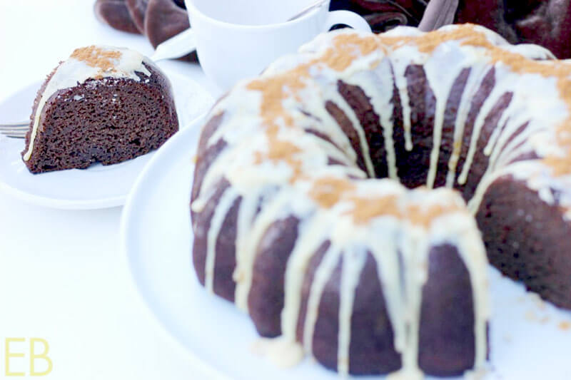 gorgeous chocolate zucchini bundt cake, drizzled with a light-colored syrup, with a piece cut out and placed on a white plate nearby