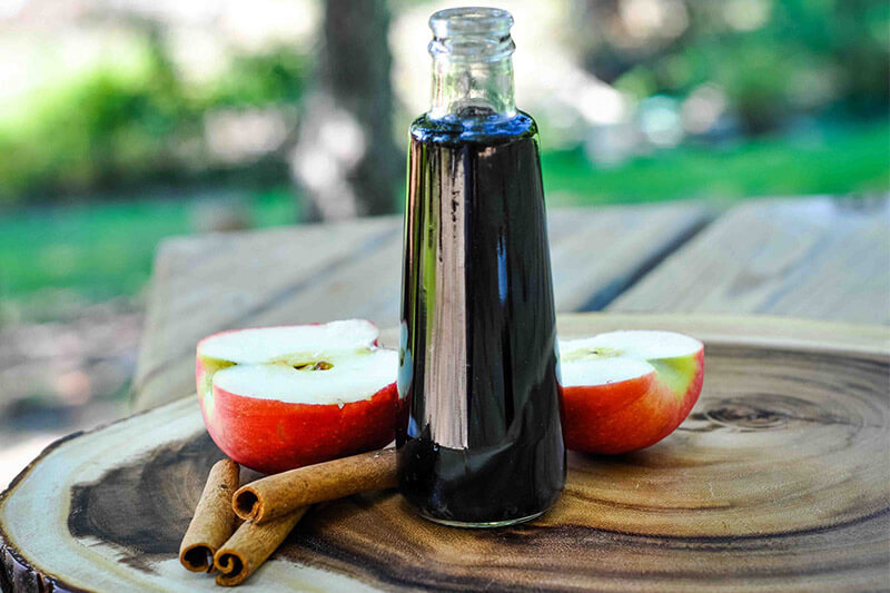 tall glass jar of apple elderberry surface, on a wooden surface, surrounded by two apple halves and cinnamon sticks