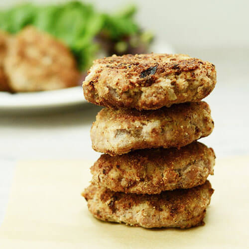 crispy sausage patties in a stack of three, with a plate of fresh greens in the background