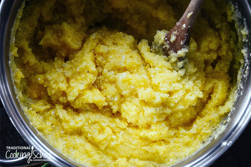 a stainless steel pot of polenta being stirred with a wooden spoon