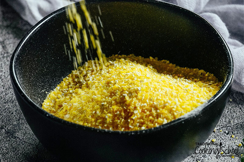 uncooked polenta grains being poured into a dark-colored bowl