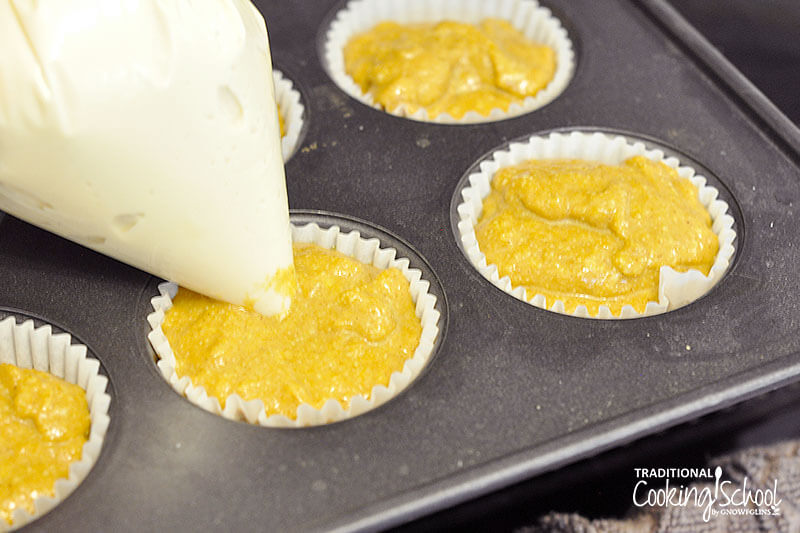 muffin tin filled with pumpkin muffin batter in muffin cups, with Ziploc bag piping cream cheese filling into each of them