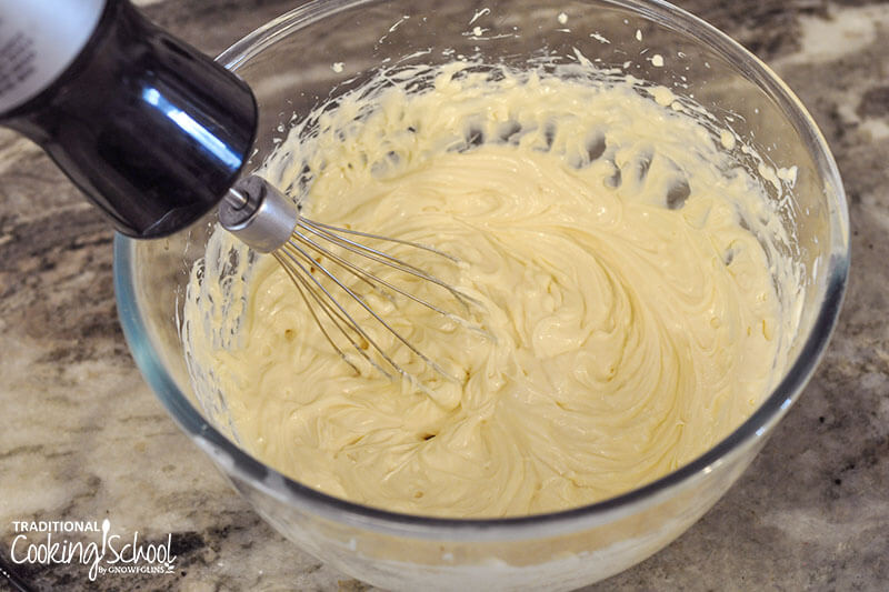 electric hand mixer beating a mixture of cream cheese, vanilla extract, and maple syrup to make cream cheese filling