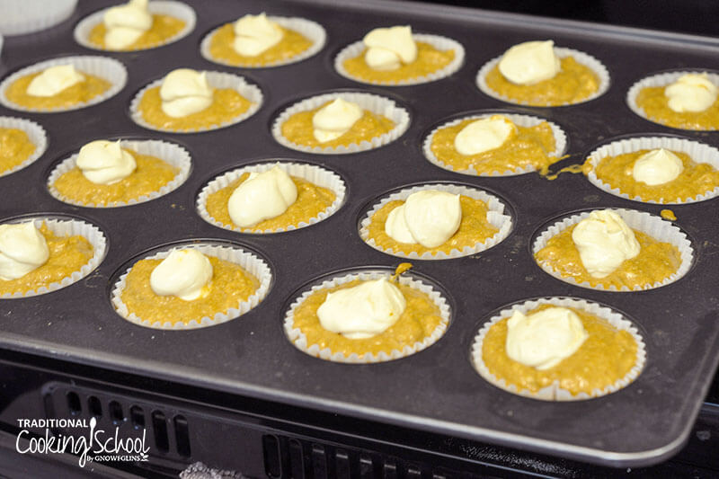 a muffin tin full of pumpkin muffin batter and cream cheese filling, ready to be baked