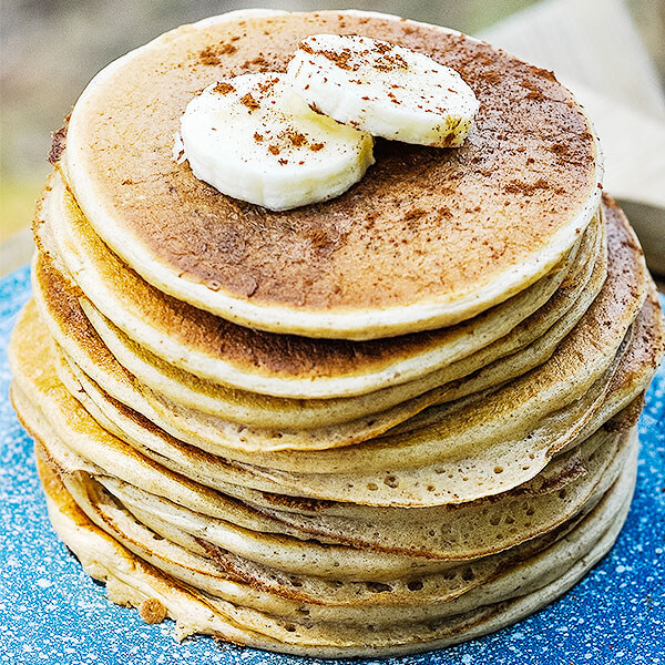 stack of fluffy, golden-brown pancakes on a blue speckled plate garnished with banana slices and a sprinkling of ground cinnamon