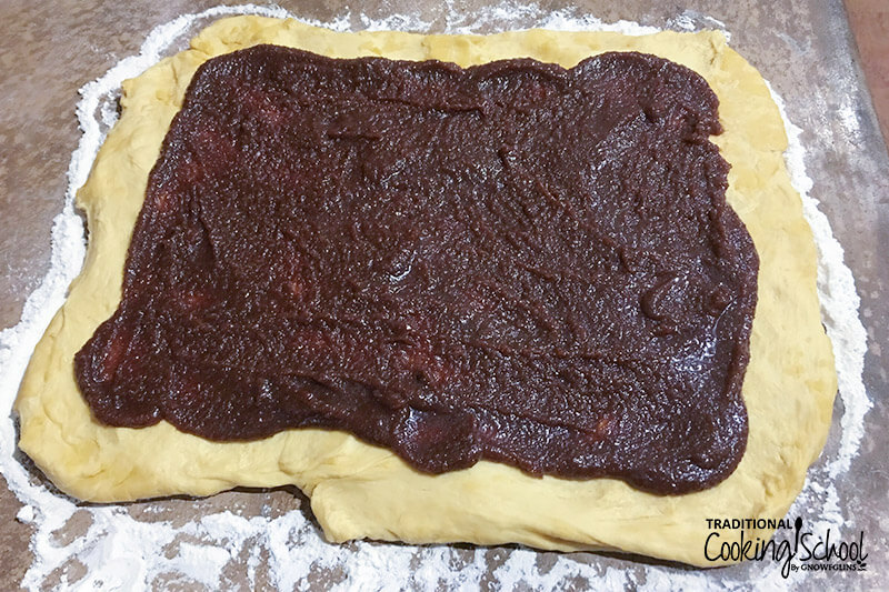 large rectangle of dough rolled out on a well-floured surface, with a dark-colored filling spread out over most of the surface