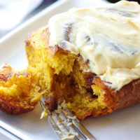 close-up shot of a sourdough pumpkin cinnamon roll slathered with cream cheese frosting, with a fork just having pulled a piece of the corner to reveal a moist, soft, tender texture inside