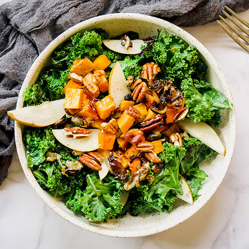 winter salad of warm kale, fresh pear slices, roasted butternut squash and sweet potato chunks, and pecans in a large bowl