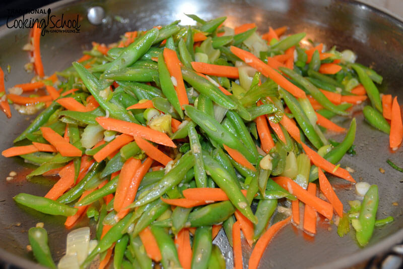 sauteing green beans, onions, and carrot shavings in a cast iron skillet