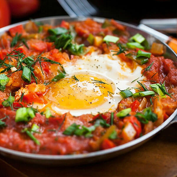 beautiful dish of shakshuka, poached eggs in tomato sauce sprinkled with fresh herbs and spices