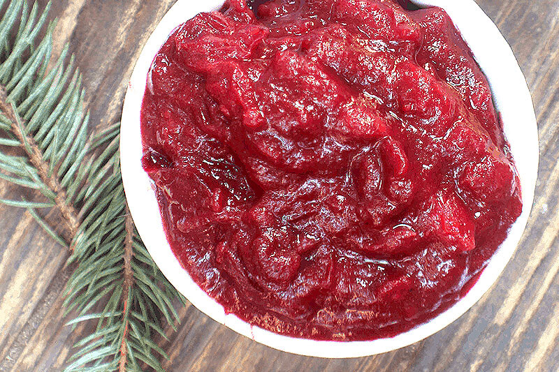 white bowl of easy cranberry sauce, on a wooden background with pine needles for decorative props