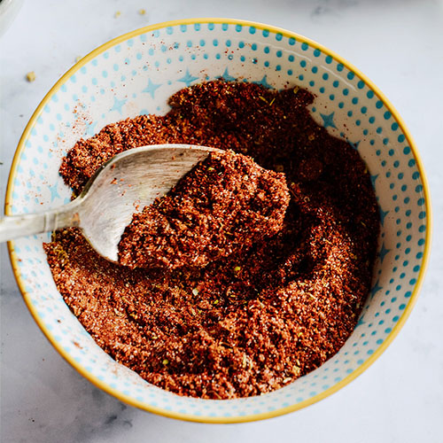 vintage spoon mixing together taco seasoning spices in a small decorative ceramic bowl