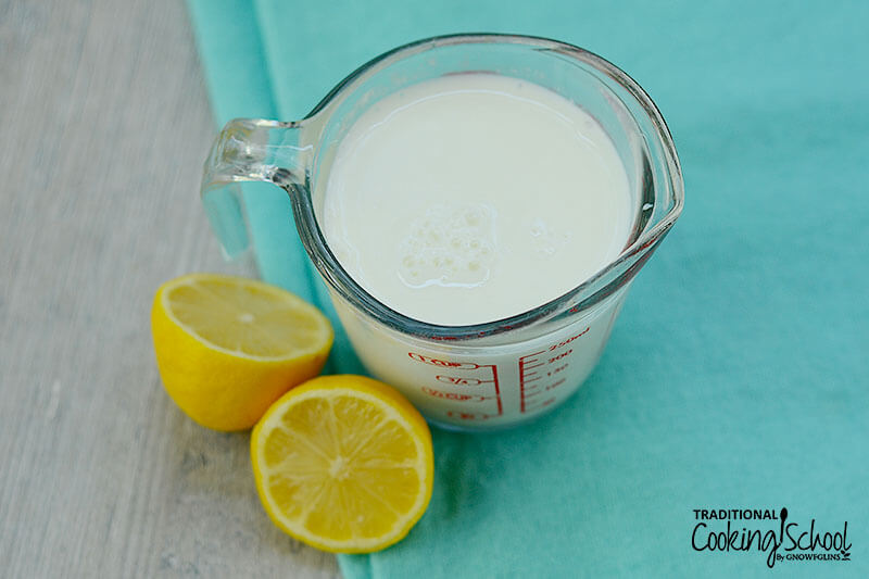 Pyrex measuring cup full of milk, next to two lemon halves on a blue cloth