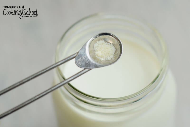 small stainless steeling measuring spoon of powdered buttermilk starter over a glass Mason jar of milk