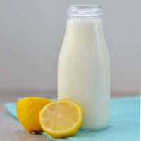 tall glass container of milk next to two lemon halves on a blue cloth