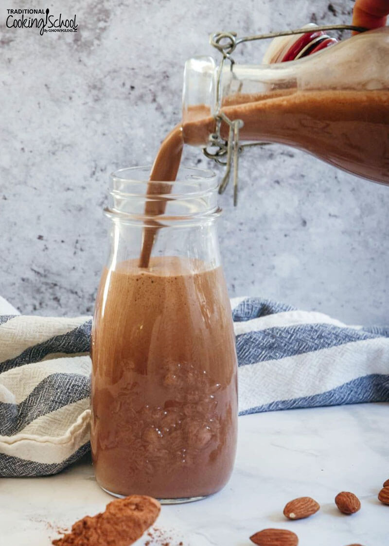 swing-top large glass bottle of chocolate almond milk pouring into a smaller glass jar for drinking