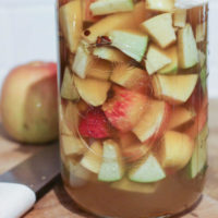 close-up shot of fermenting raw apple cider vinegar in a glass jar, involving apple chunks submerged in a sugar water solution