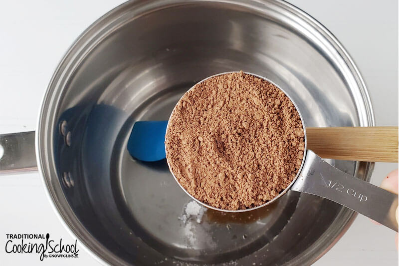 1/2 cup of cocoa powder held over a stainless steel pot with melted coconut oil in the bottom