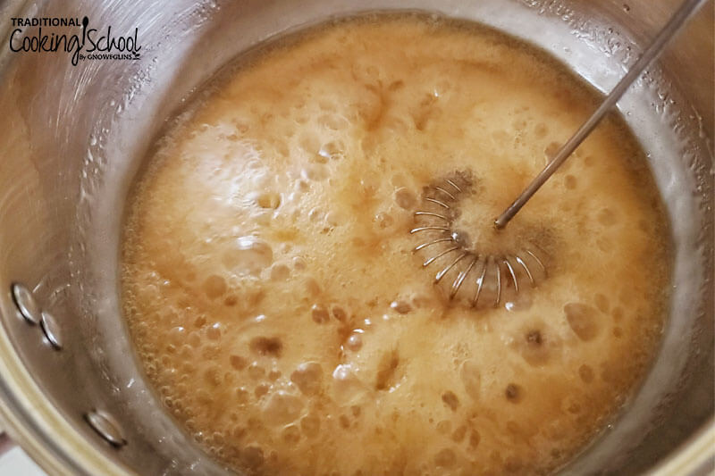 whisk mixing together honey and coconut oil as it is brought to a boil