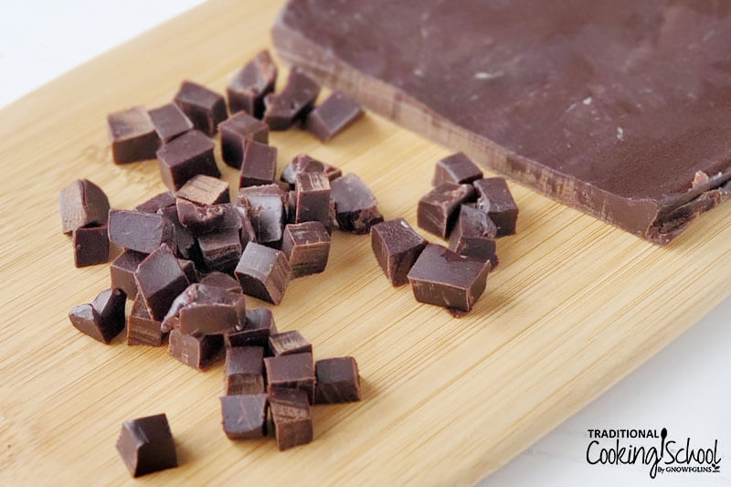 slab of homemade chocolate on a wooden cutting board in the process of being cut into chips