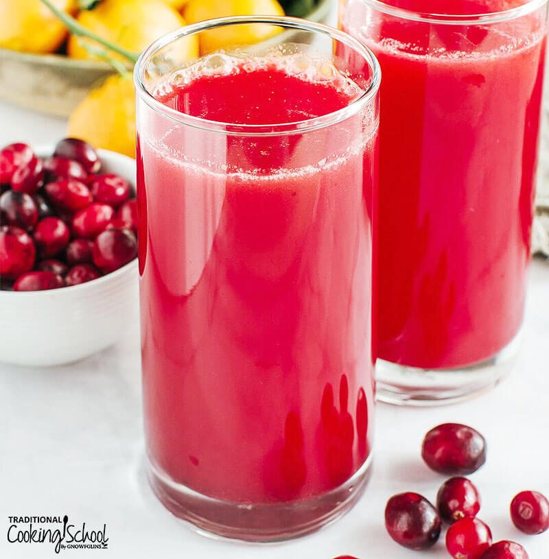 two glasses of homemade cranberry juice with oranges and fresh cranberries in the background