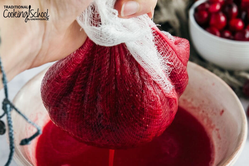 woman's hand squeezing cranberry juice out from the pulp with a cheesecloth