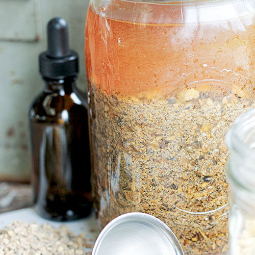 amber glass dropper bottle next to a half gallon glass jar full of an herbal mixture