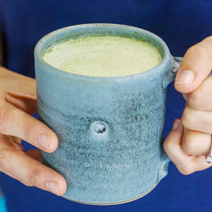 woman's hands holding a matcha latte in a ceramic mug