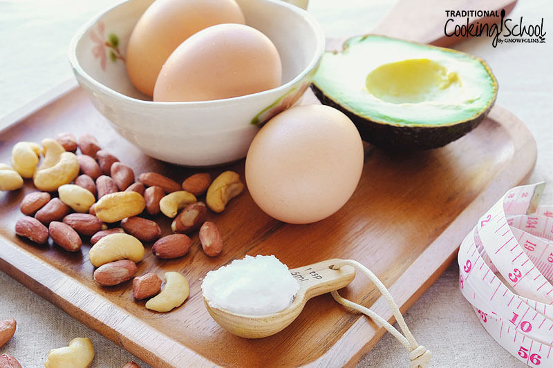 wooden cutting board with healthy ingredients to boost your immune system on it: cashews and almonds, eggs, half of an avocado, and coconut oil