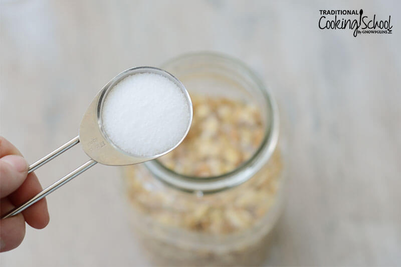close-up shot of a teaspoon of sea salt over a glass Mason jar full of walnuts and water