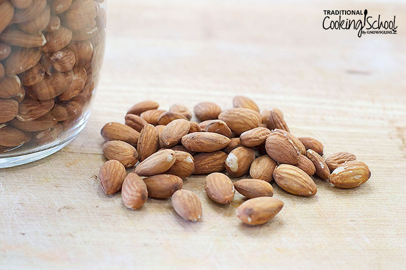 soaked and dehydrated almonds on a cutting board next to more almonds in a glass jar