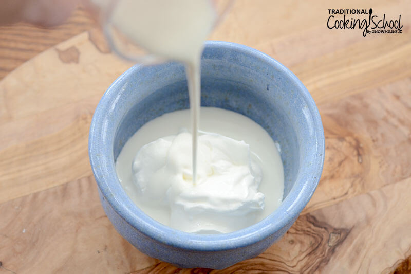 pouring heavy cream into a small blue ceramic bowl of sour cream