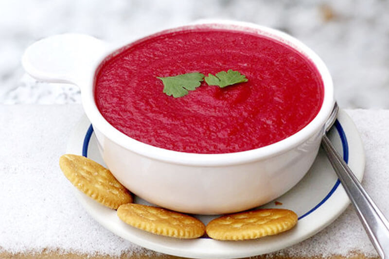 bright pink carrot beet blended soup in a small bowl with three crackers on a plate