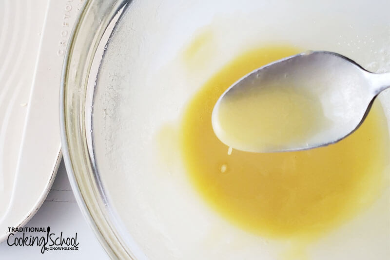 spoonful of white chocolate candy mixture over a clear glass bowl of more white chocolate