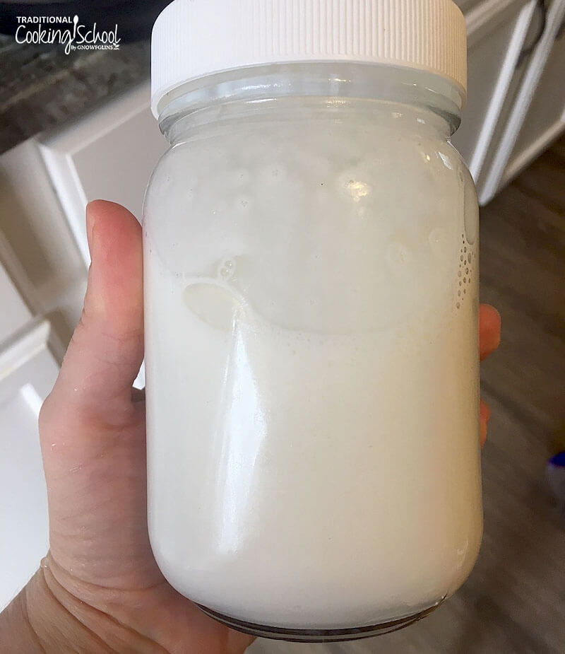 woman's hand holding a glass jar of dairy-free milk alternative