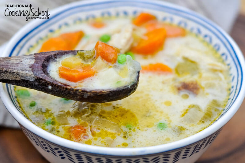 Bowlful and spoonful of savory chicken pot pie soup. There are carrots and peas visible.