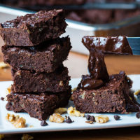 stack of brownies on a plate with a knife frosting an additional brownie