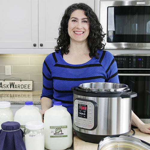 smiling woman standing in a kitchen with gallons of raw milk and and Instant Pot in front of her