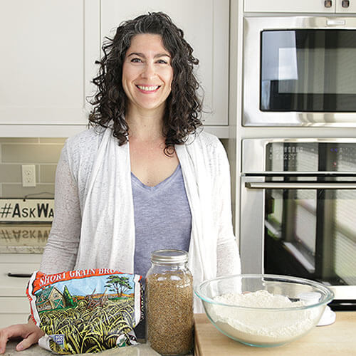 woman smiling in a kitchen with whole grains and a bowl of flour in front of her