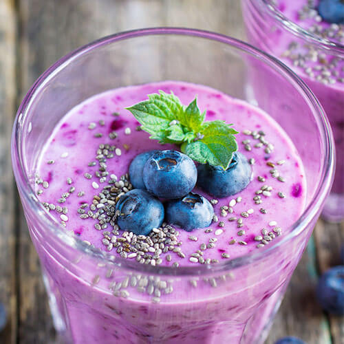 bright purple drink in a glass, garnished with blueberries, chia seeds, and a sprig of mint