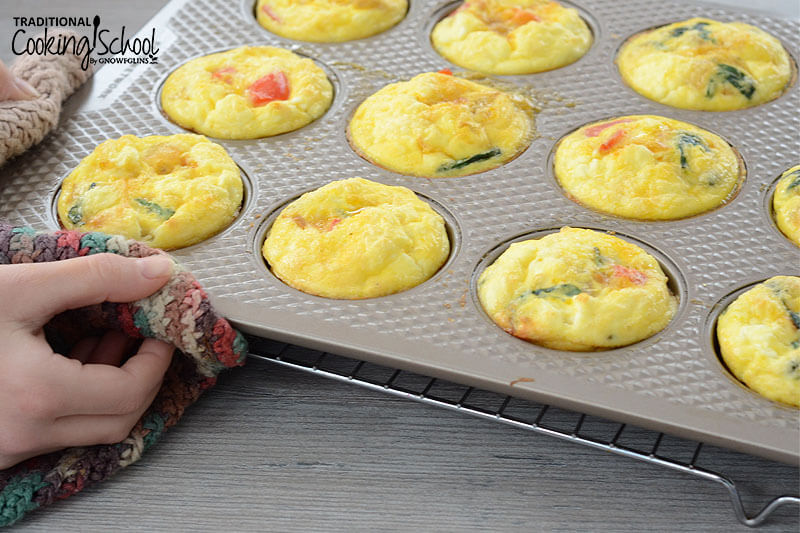 hands using hot pads to handle a muffin tin of mini frittatas