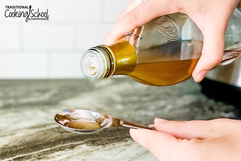 woman's hand pouring a bottle of apple cider vinegar into a measuring spoon