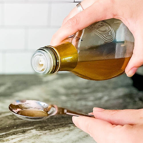 woman's hand pouring a bottle of apple cider vinegar into a measuring spoon