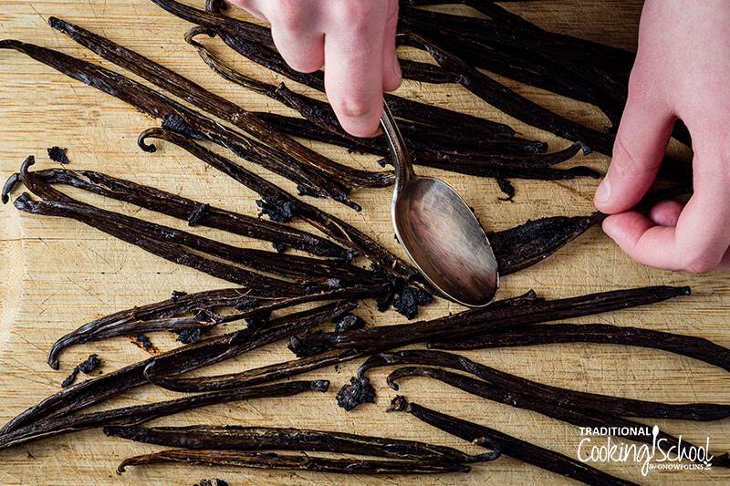 hands scooping vanilla seeds out of a vanilla bean with a spoon
