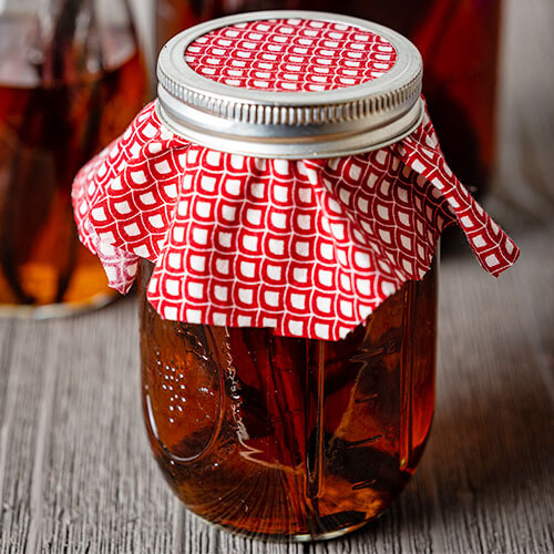 small jar of vanilla beans and vodka covered with a red cloth and secured with a metal band